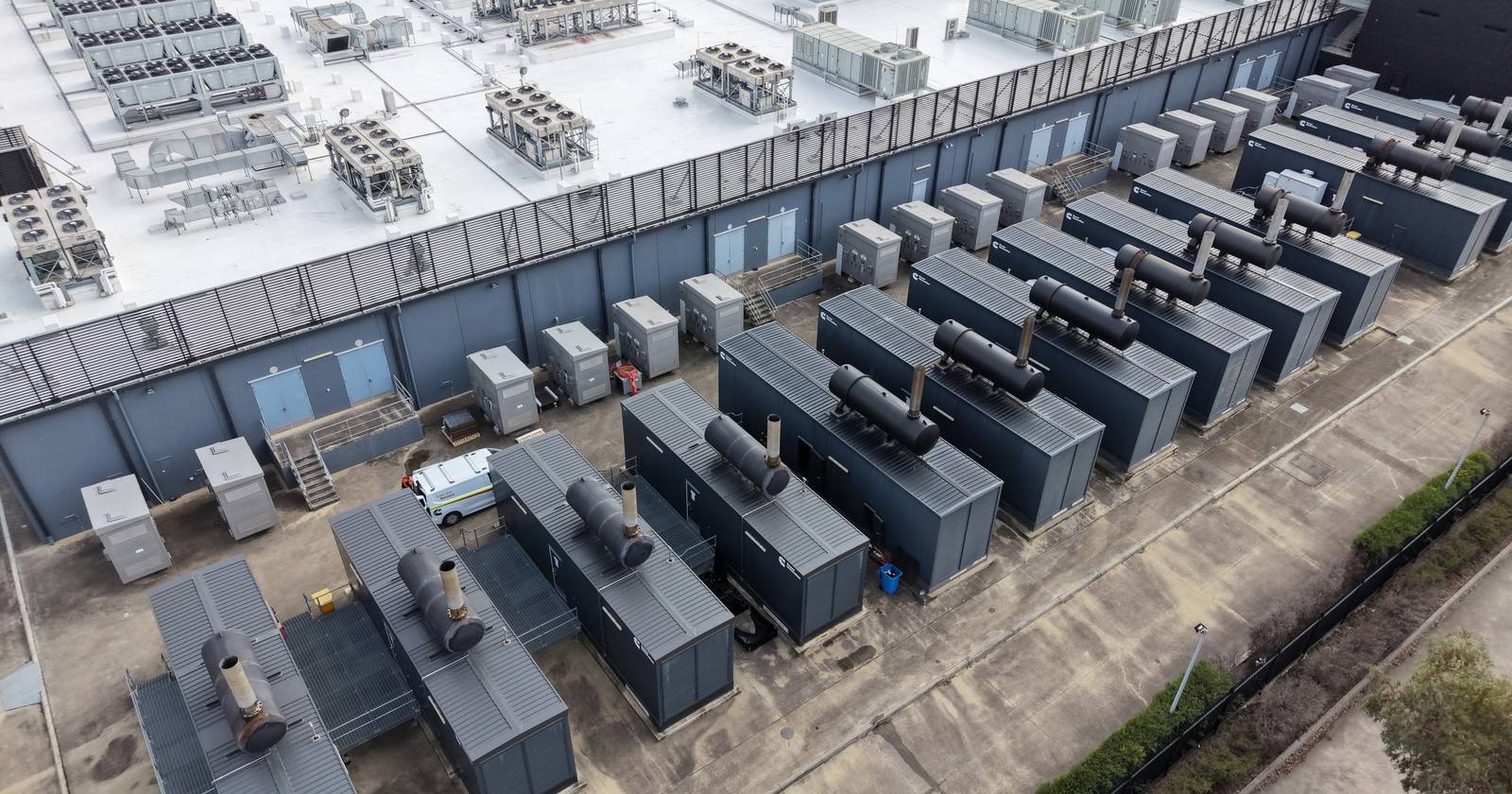 Aerial view of a data centre showing rooftop cooling plant and a line of containerised standby generators