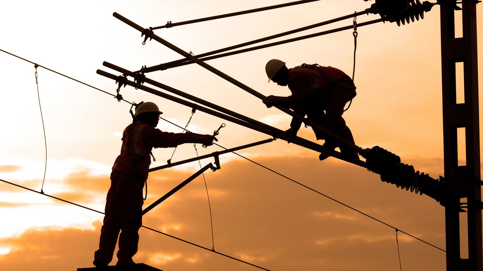 A field crew in hi-vis securing work on an exposed structure as a thunderstorm approaches.